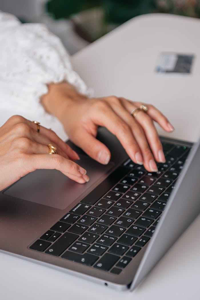 hero-gallery-01 Hands of a woman typing on a laptop keyboard indoors, showcasing rings and fashion.