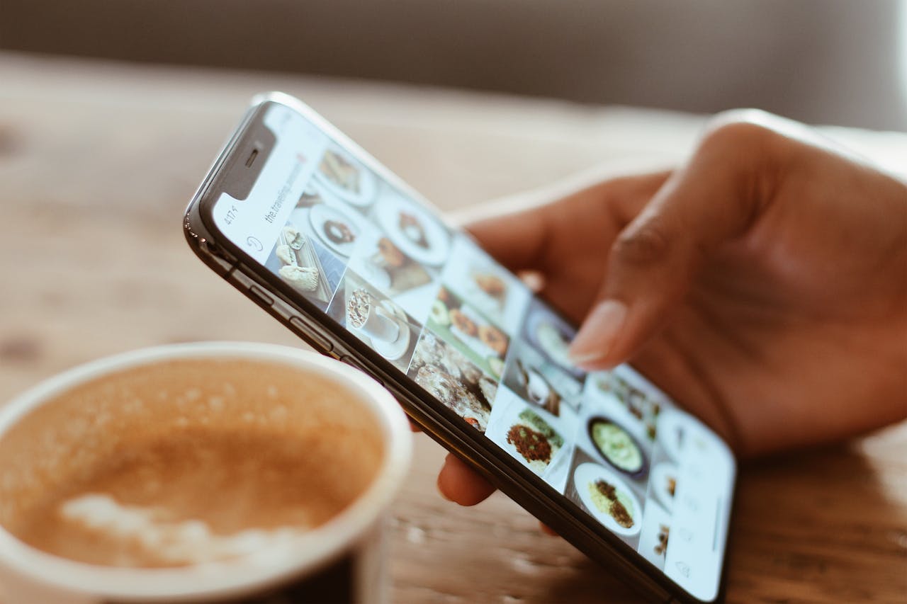 hero-gallery-02 Hand browsing social media photos on a smartphone next to a cup of coffee indoors.